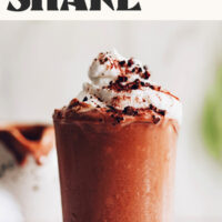 Glass of our Vegan Jamocha Shake recipe topped with coconut whipped cream and text above it that says maple-sweetened