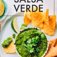 Bowl of roasted salsa verde on a platter with tortilla chips and lime wedges