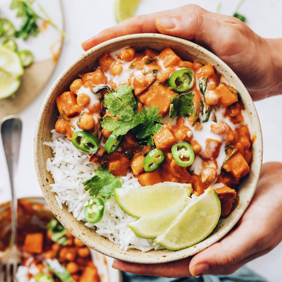 Holding a bowl of roasted red pepper chickpea curry topped with cilantro and limes