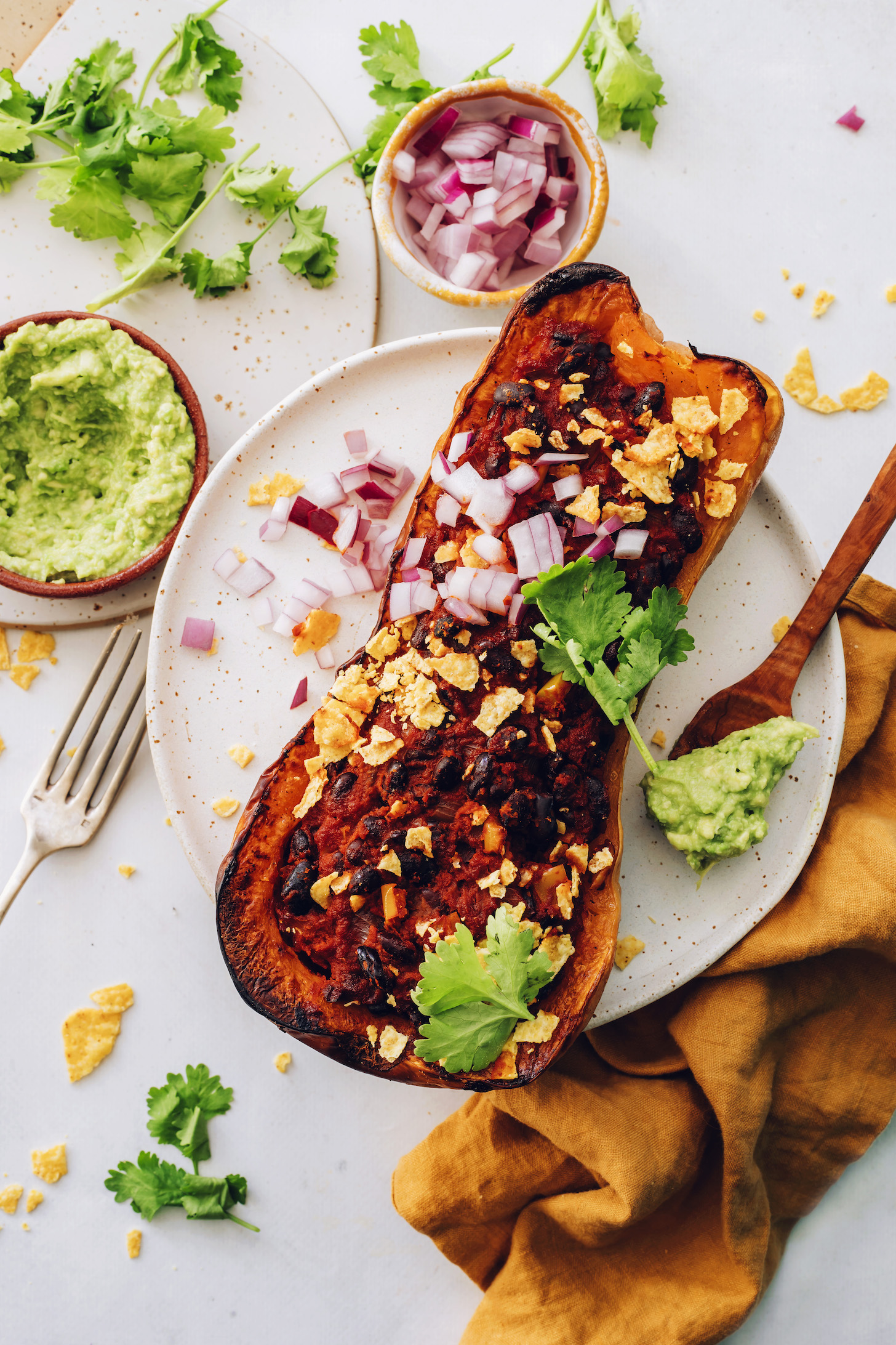 Overhead photo of a stuffed squash topped with tortilla chips, cilantro, red onion, and guacamole