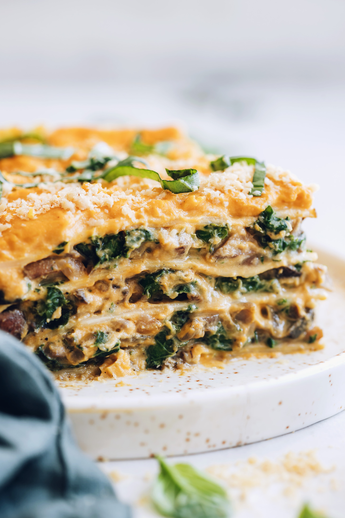 Close up shot of a slice of butternut squash lasagna topped with vegan parmesan and fresh basil