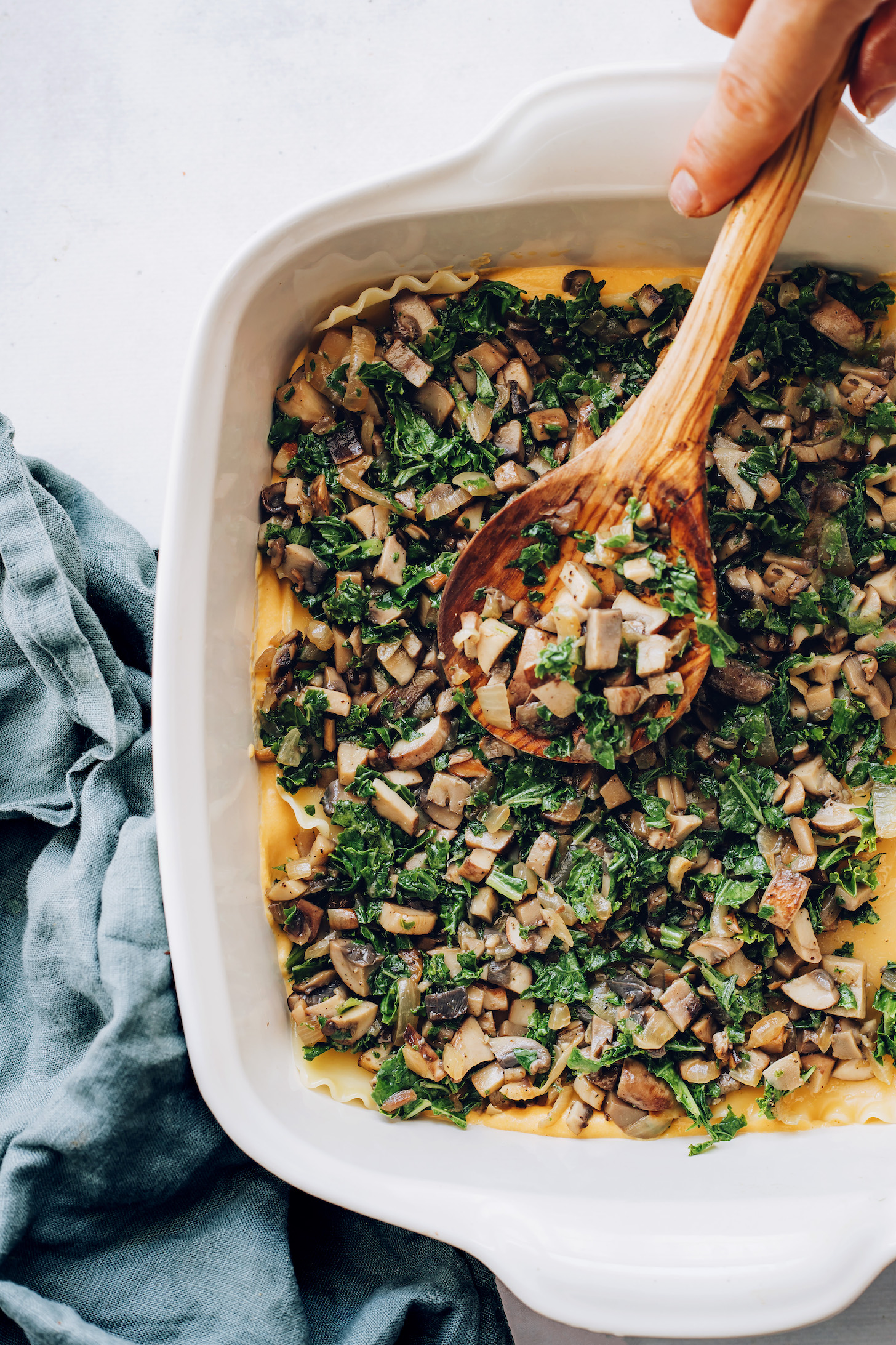 Layering mushroom kale filling over lasagna noodles
