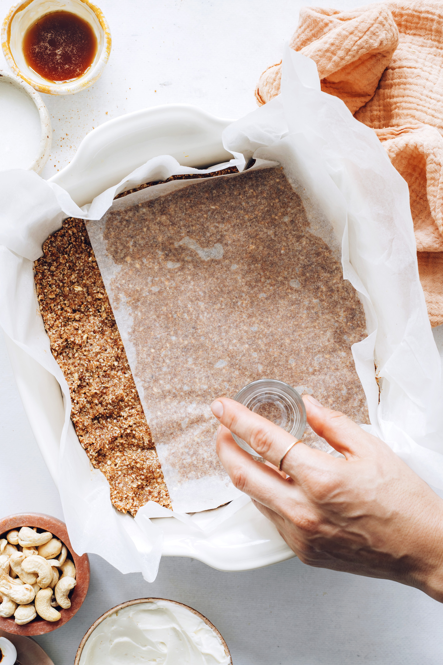 Pressing crust into a pan using a drinking glass over parchment paper