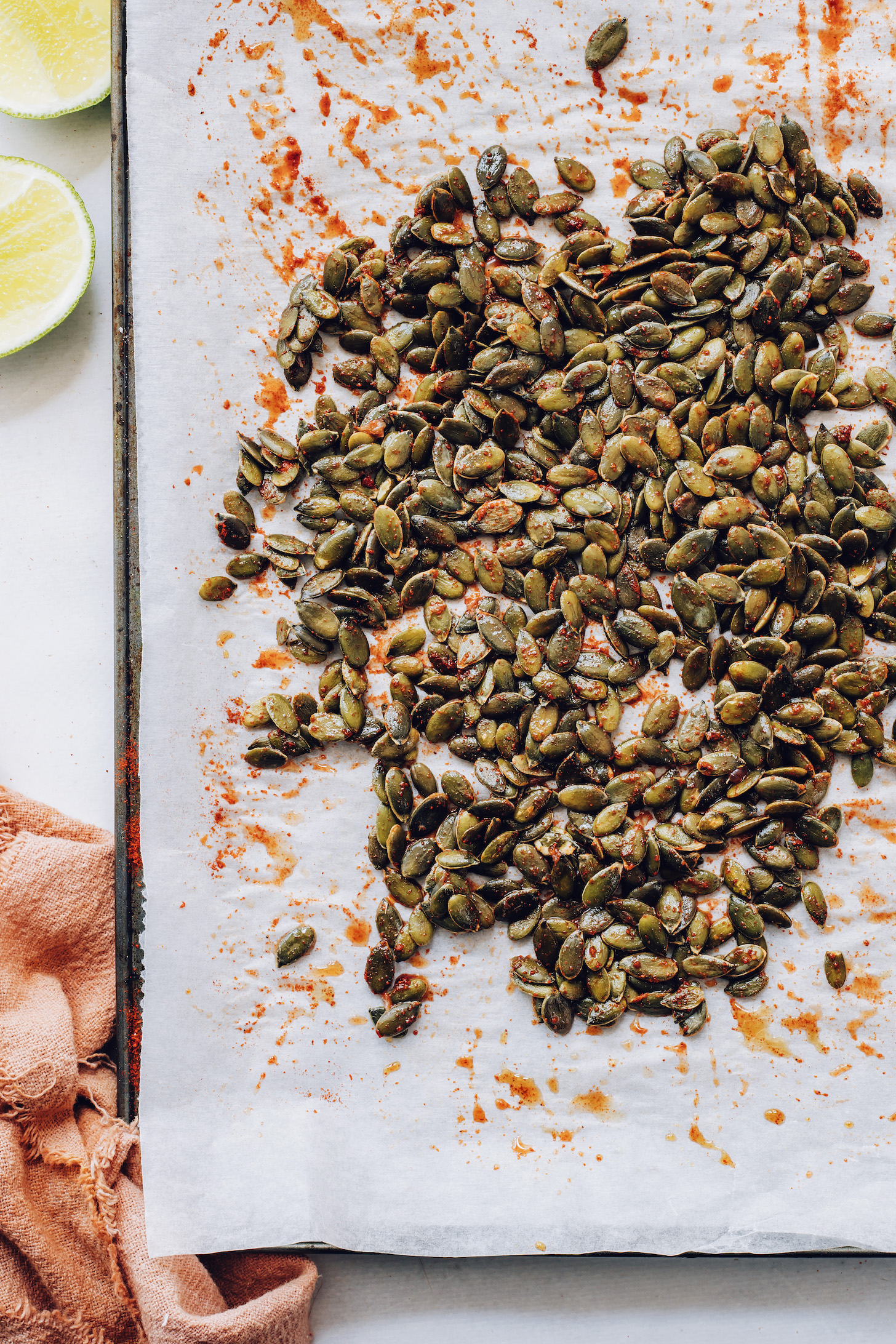 Baking sheet of raw pepitas tossed with maple syrup, lime juice, and spices