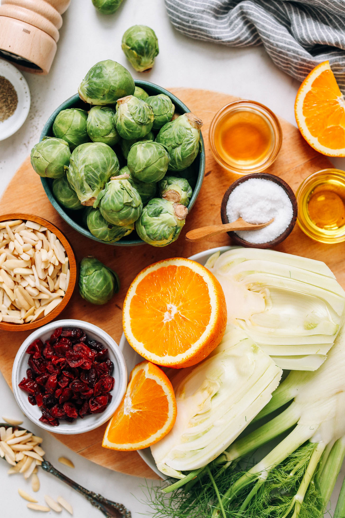 Cutting board with Brussels sprouts, almonds, cranberries, orange, fennel, salt, olive oil, and apple cider vinegar