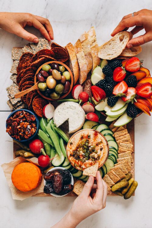 Hands grabbing snacks off a vegan charcuterie board