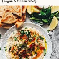 Plate of charred serrano white bean dip with pita bread and serrano peppers around it