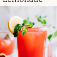 Glass of easy homemade strawberry lemonade with fresh lemon and mint on the side