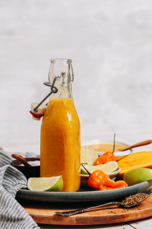 Bottle of mango habanero hot sauce next to limes, habaneros, and mango