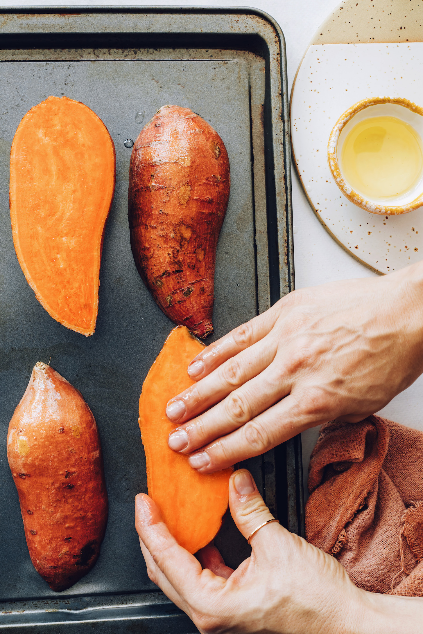 Rubbing oil onto halved sweet potatoes on a baking sheet