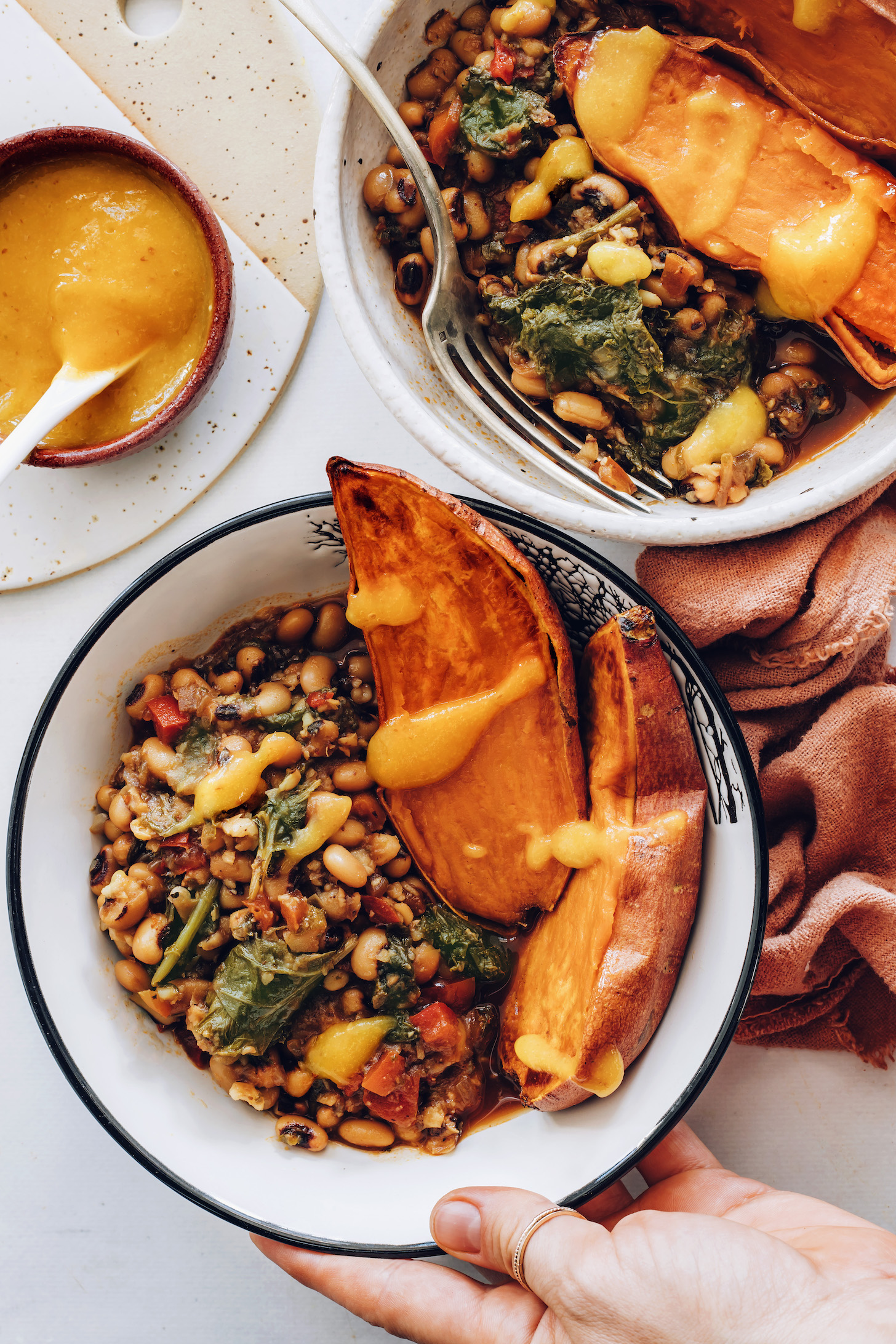 Holding a black eyed peas and greens nourish bowl with sweet potato and hot sauce