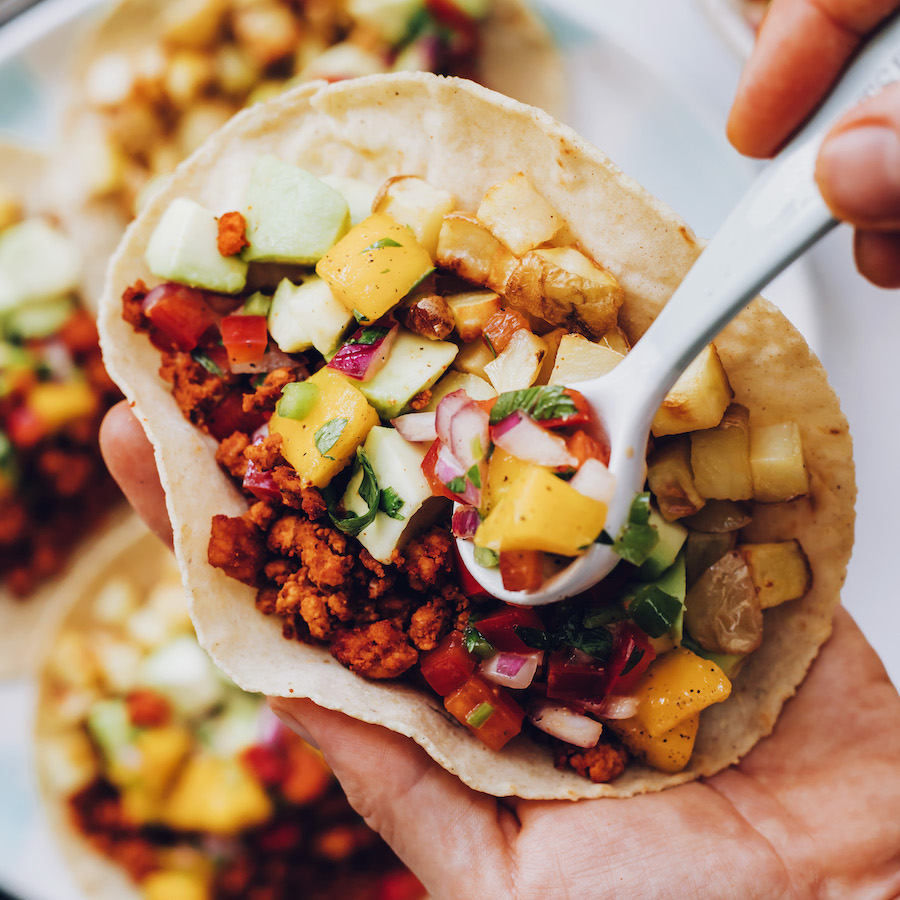 Using a spoon to add mango salsa to a breakfast taco