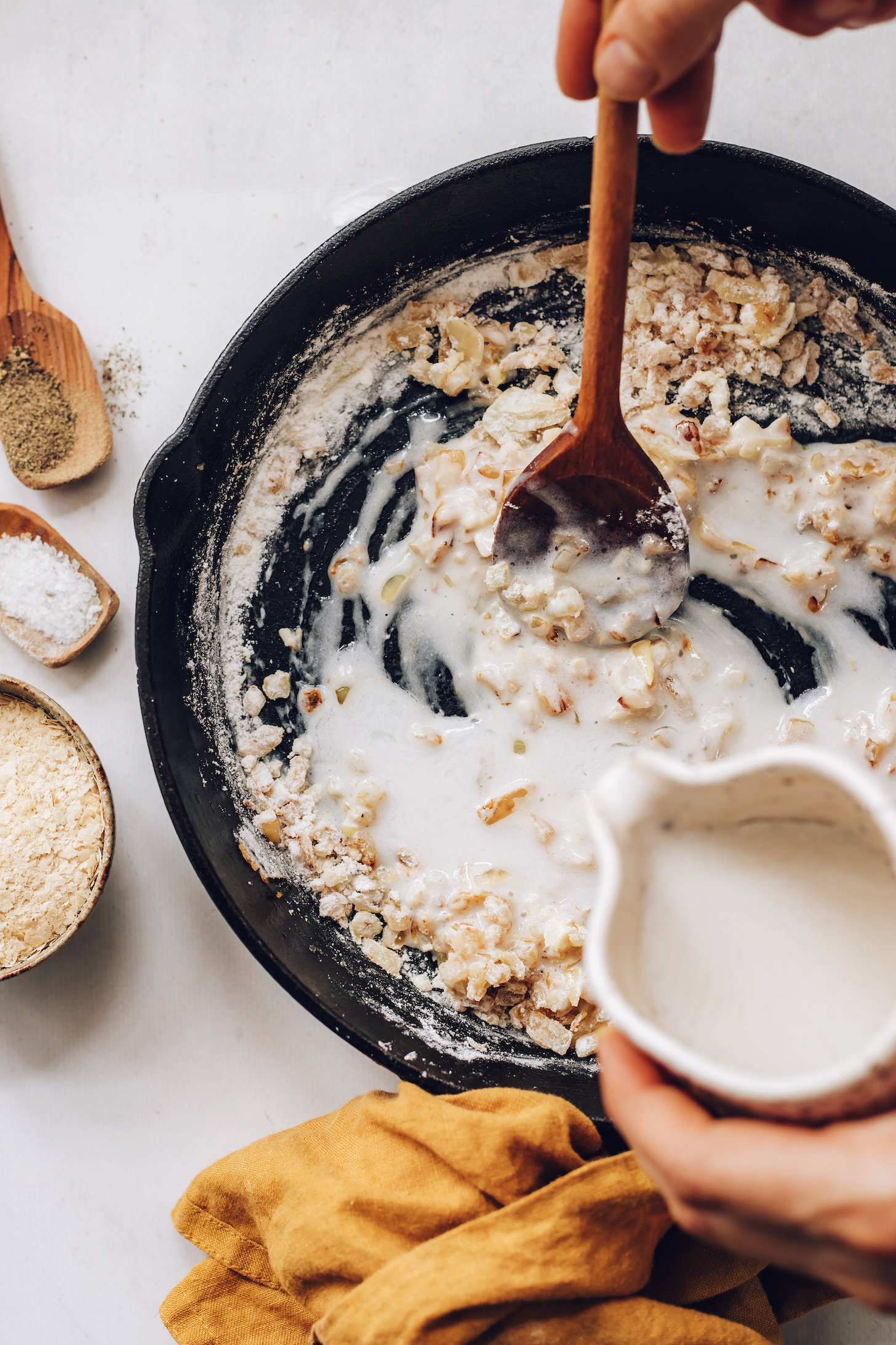 Pouring coconut milk into a skillet of sautéed onions, garlic, and cornstarch