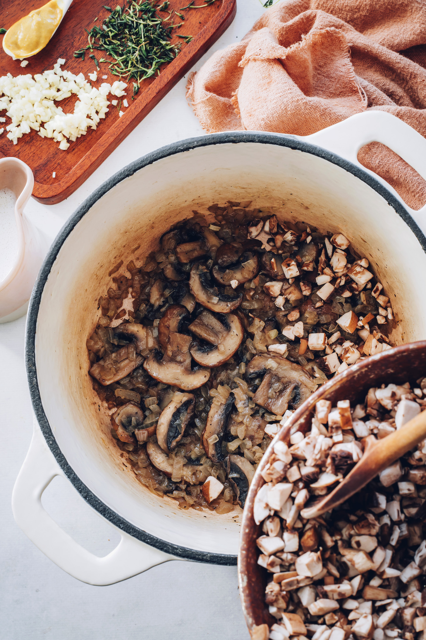 Adding chopped mushrooms to a pot of sautéed onions and sliced mushrooms
