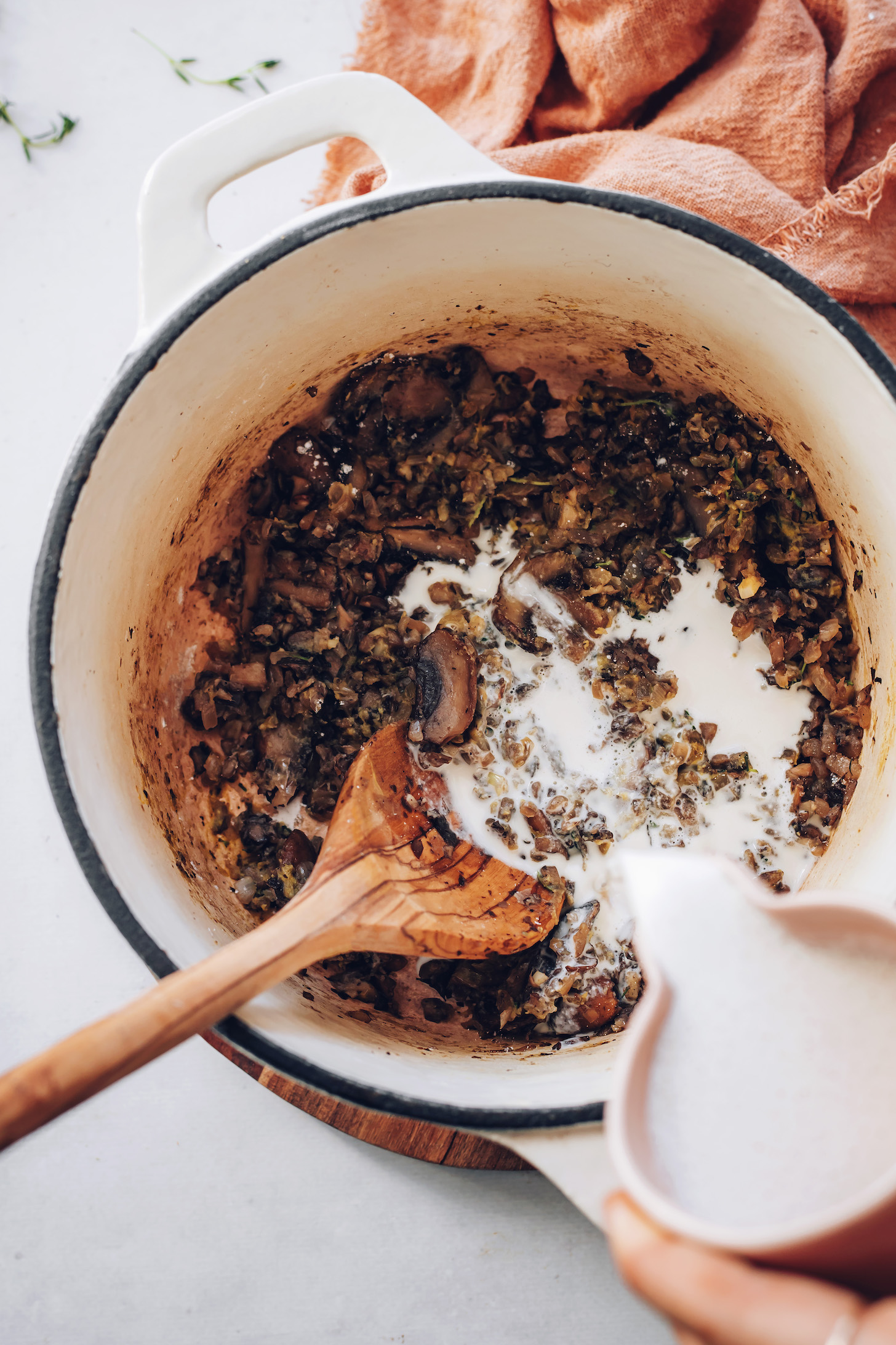 Pouring cashew cream over sautéed mushrooms and onions