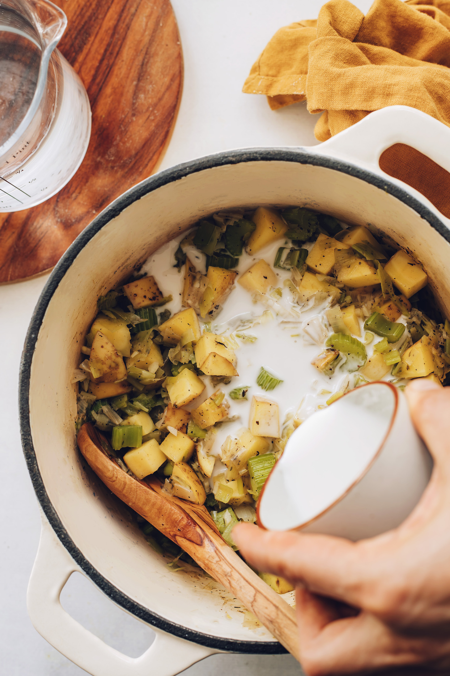 Adding light coconut milk to a pot for creamy dairy-free potato leek soup
