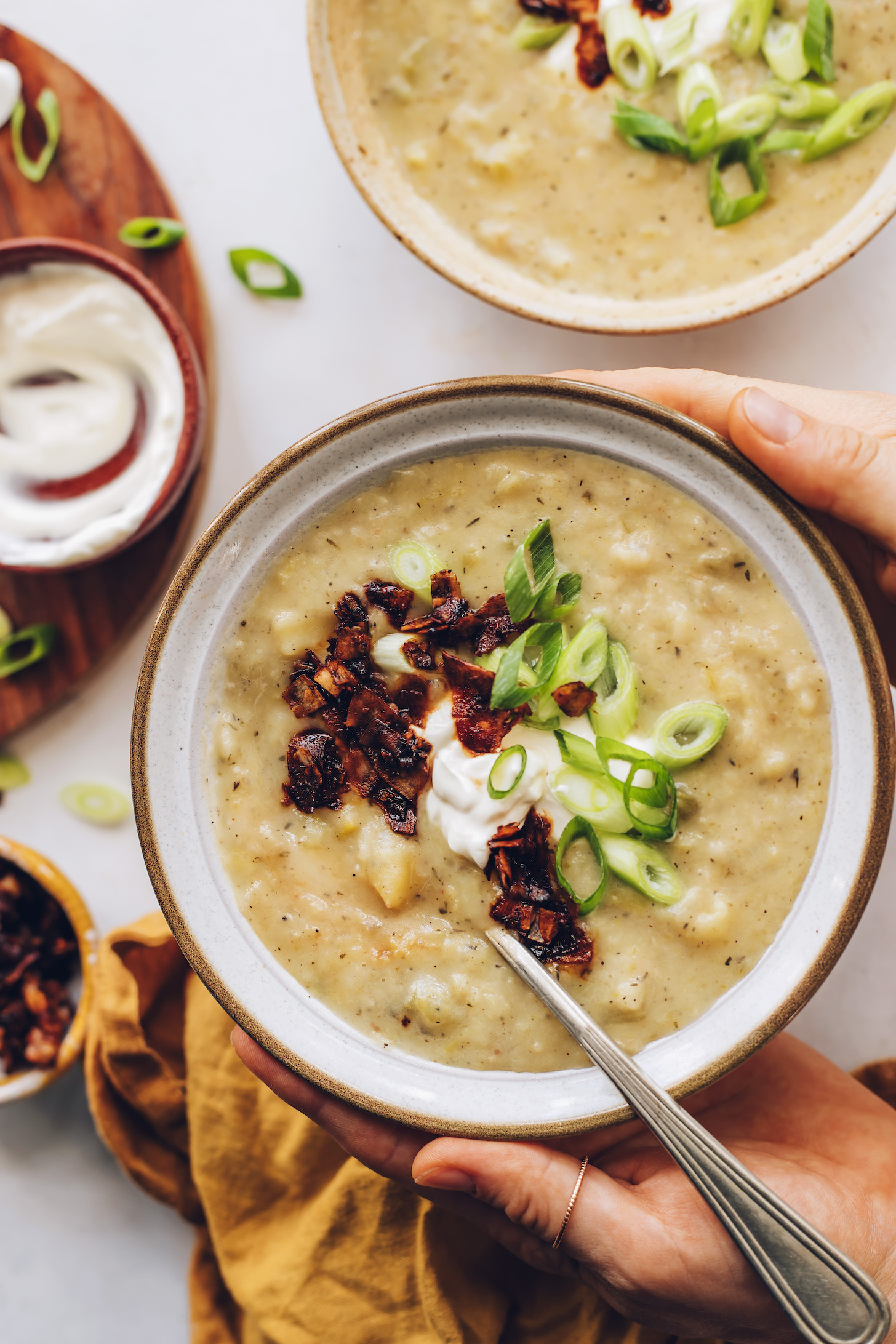 Holding a bowl of potato leek soup garnished with green onion, sour cream, and coconut bacon