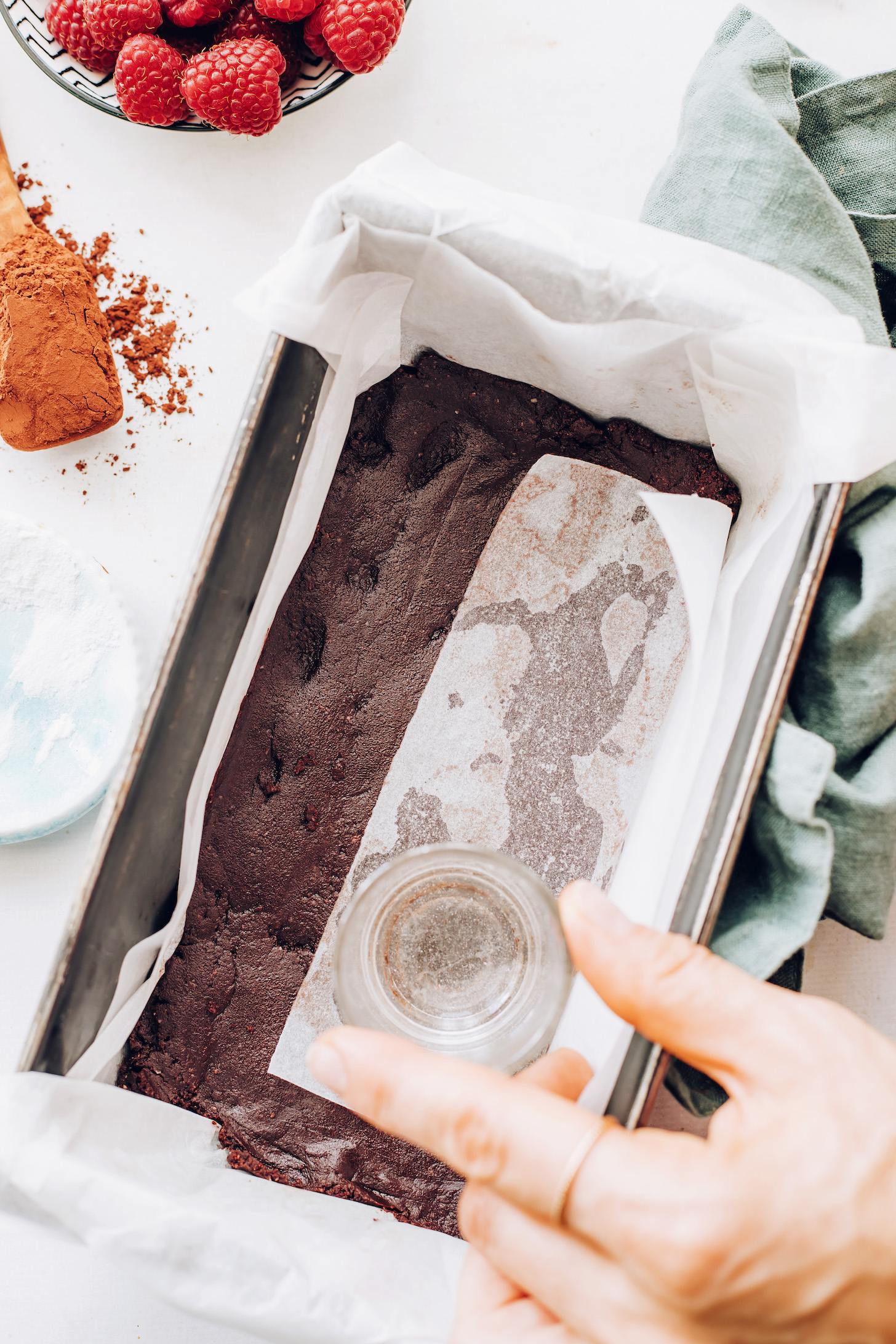 Using a cup over parchment paper to pack chocolate crust into a loaf pan