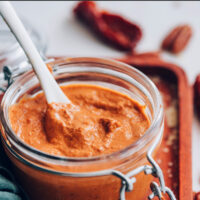 Jar of vegan and gluten-free creamy chipotle pecan pesto with a spoon in it