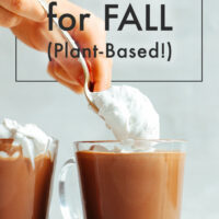 Mug of vegan hot chocolate with a hand scooping vegan whipped cream into it
