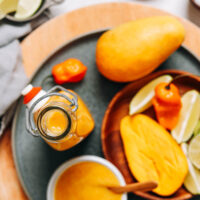 Jar of zesty mango habanero hot sauce with mango slices, lime wedges, and habanero peppers surrounding it