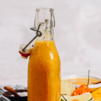 Jar of zesty mango habanero hot sauce with habanero peppers and lime wedges beside it