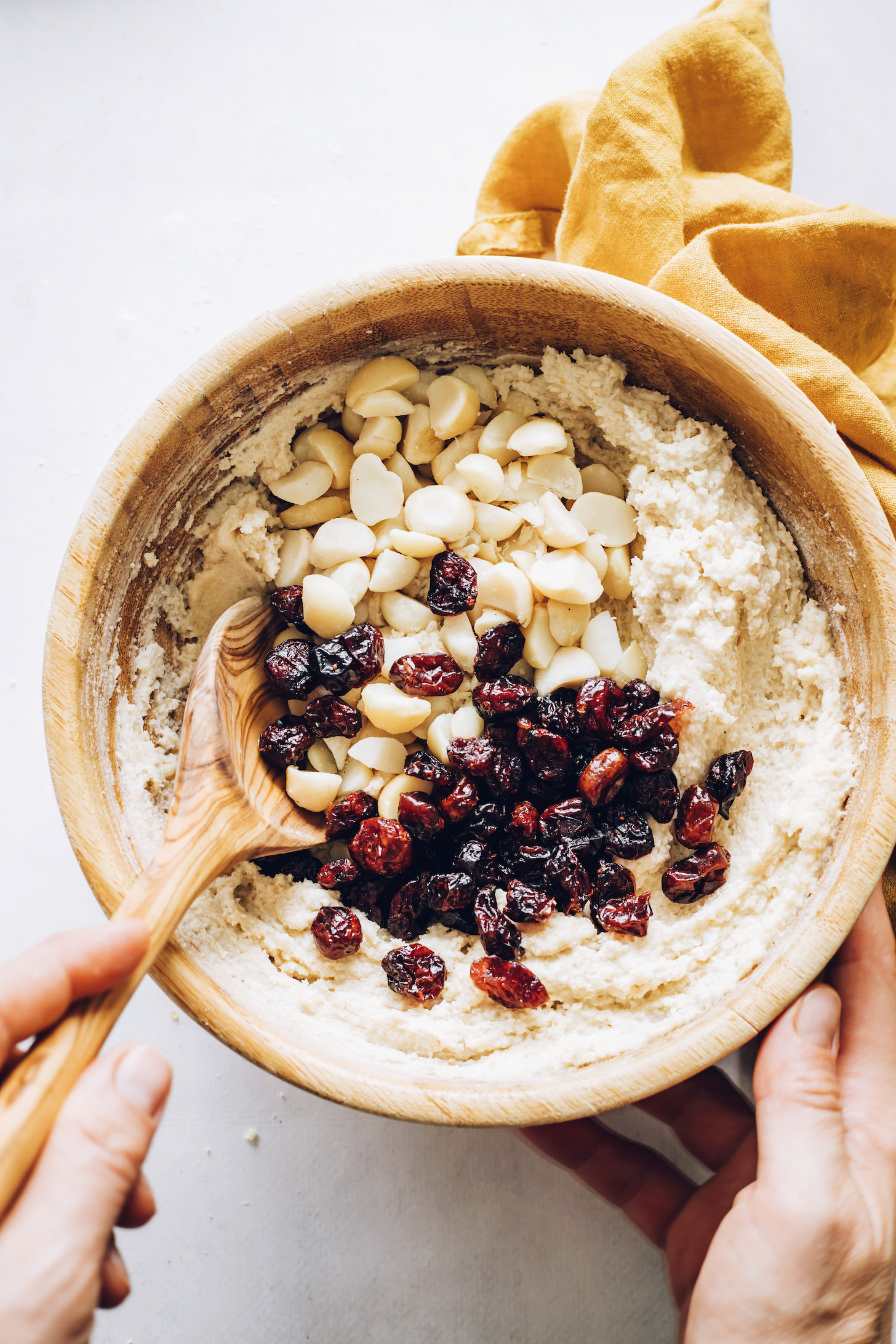 Stirring macadamia nuts and dried cranberries into fluffy cookie dough
