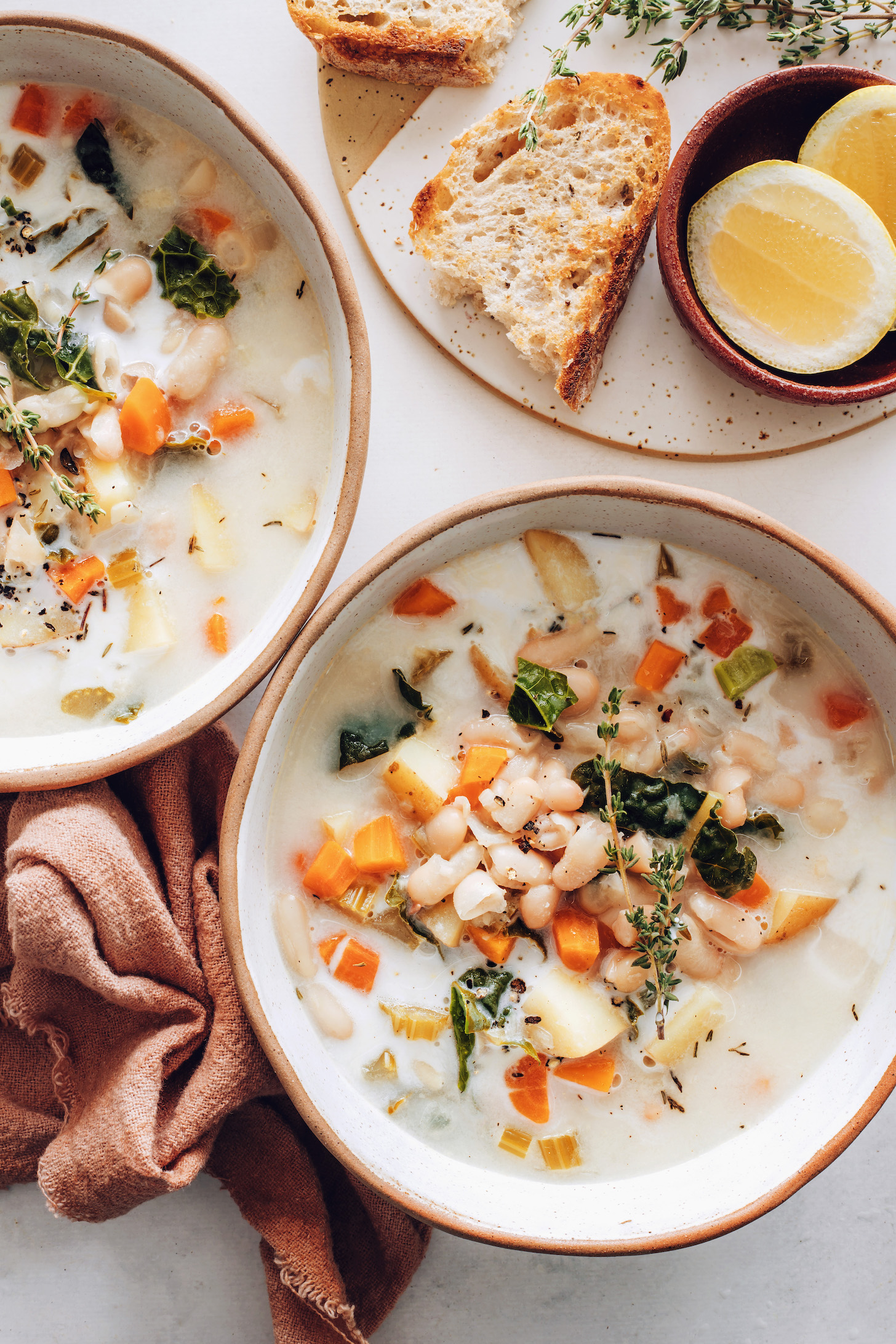 Lemons, bread, and thyme beside two bowls of vegan white bean soup