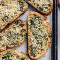 Close up shot of golden brown slices of vegan garlic bread on a baking sheet