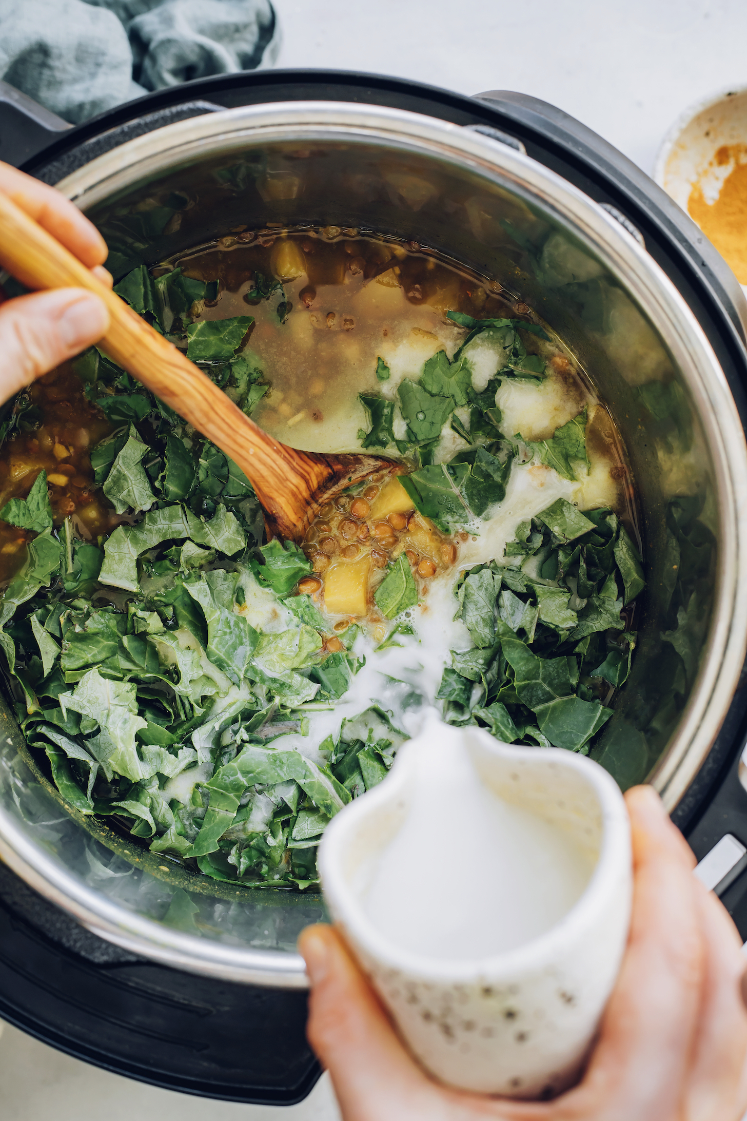Pouring coconut milk into an Instant Pot of lentil soup