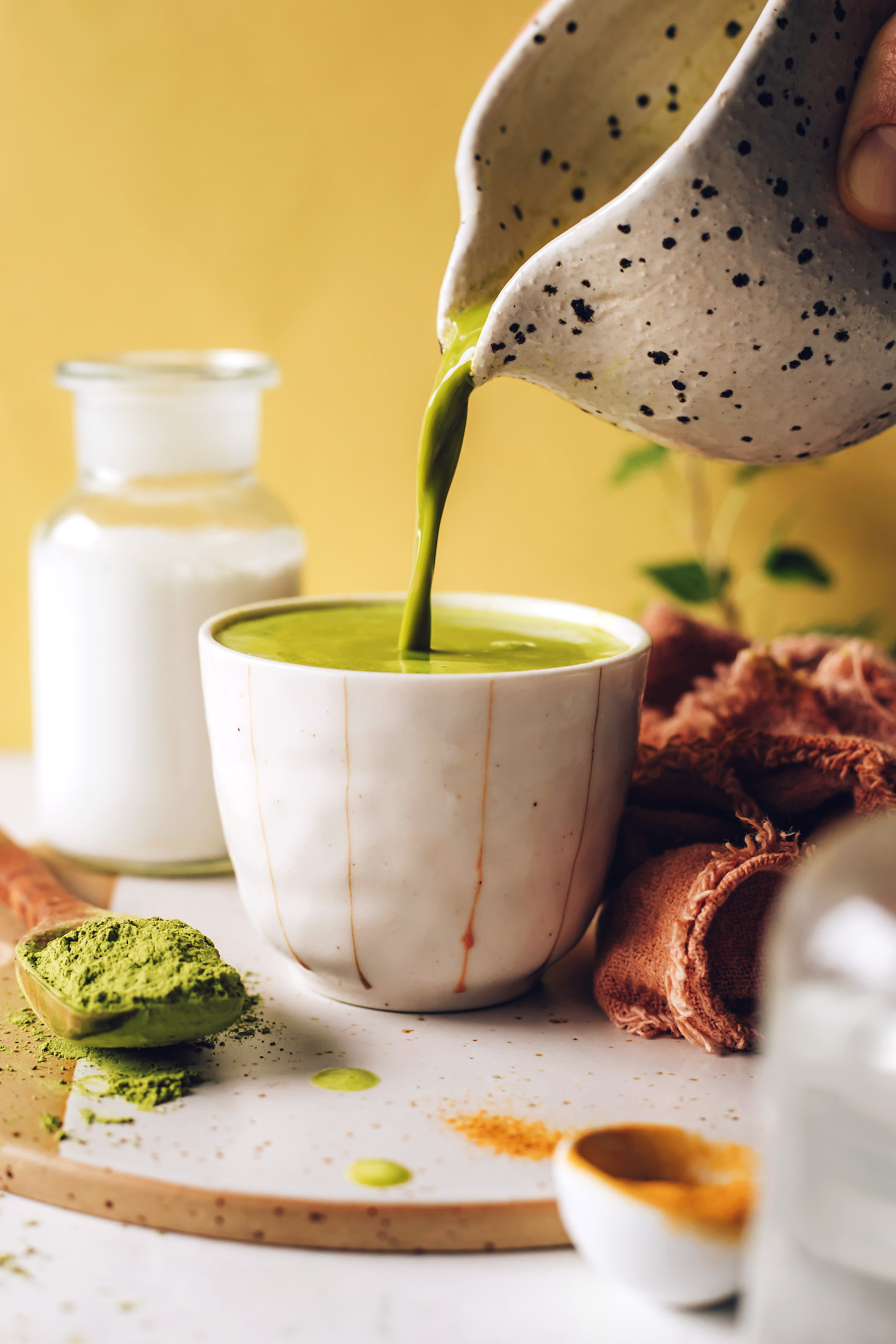 Pouring a hot golden matcha latte into a mug