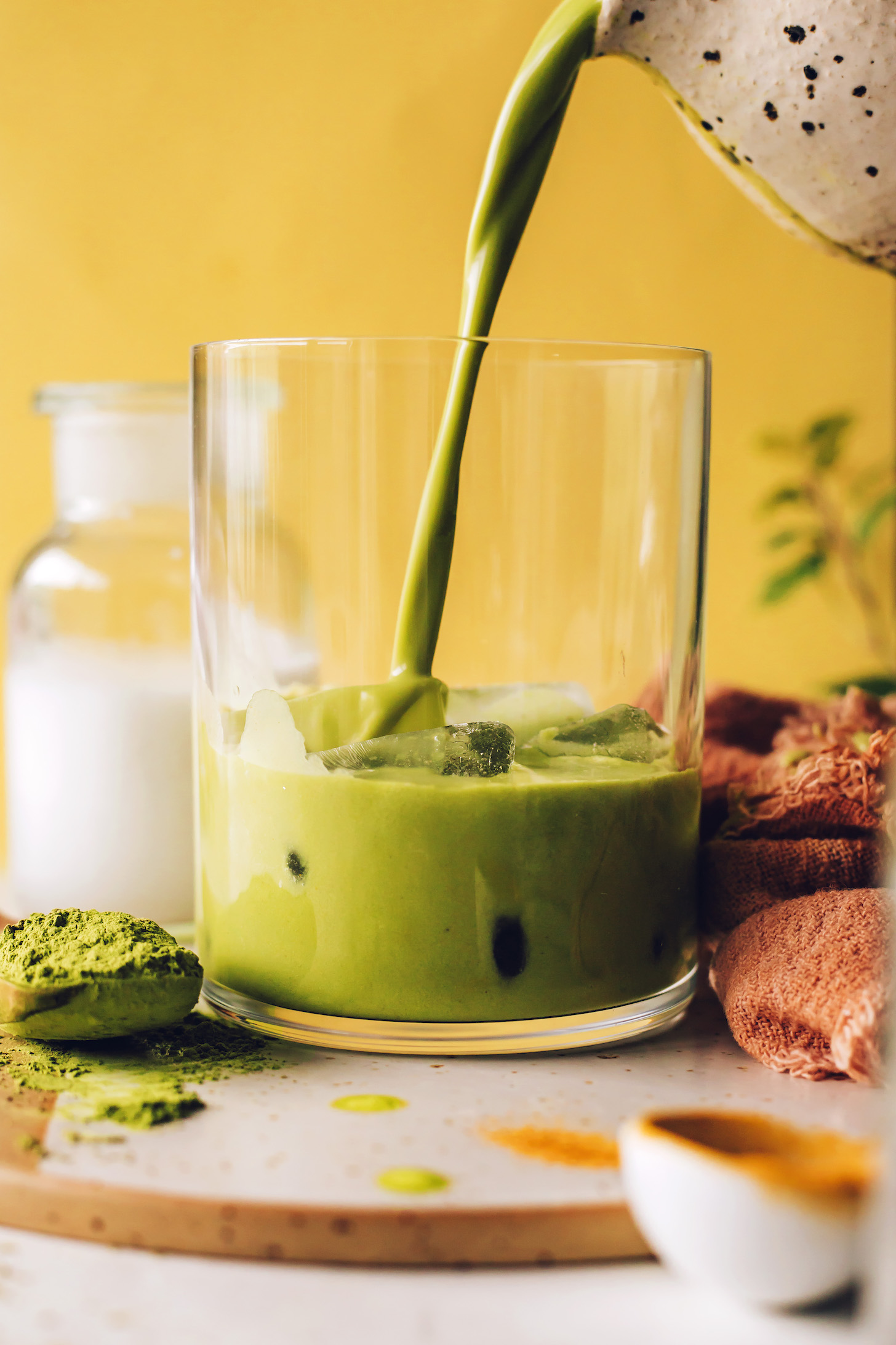 Pouring a golden matcha latte over ice cubes in glass