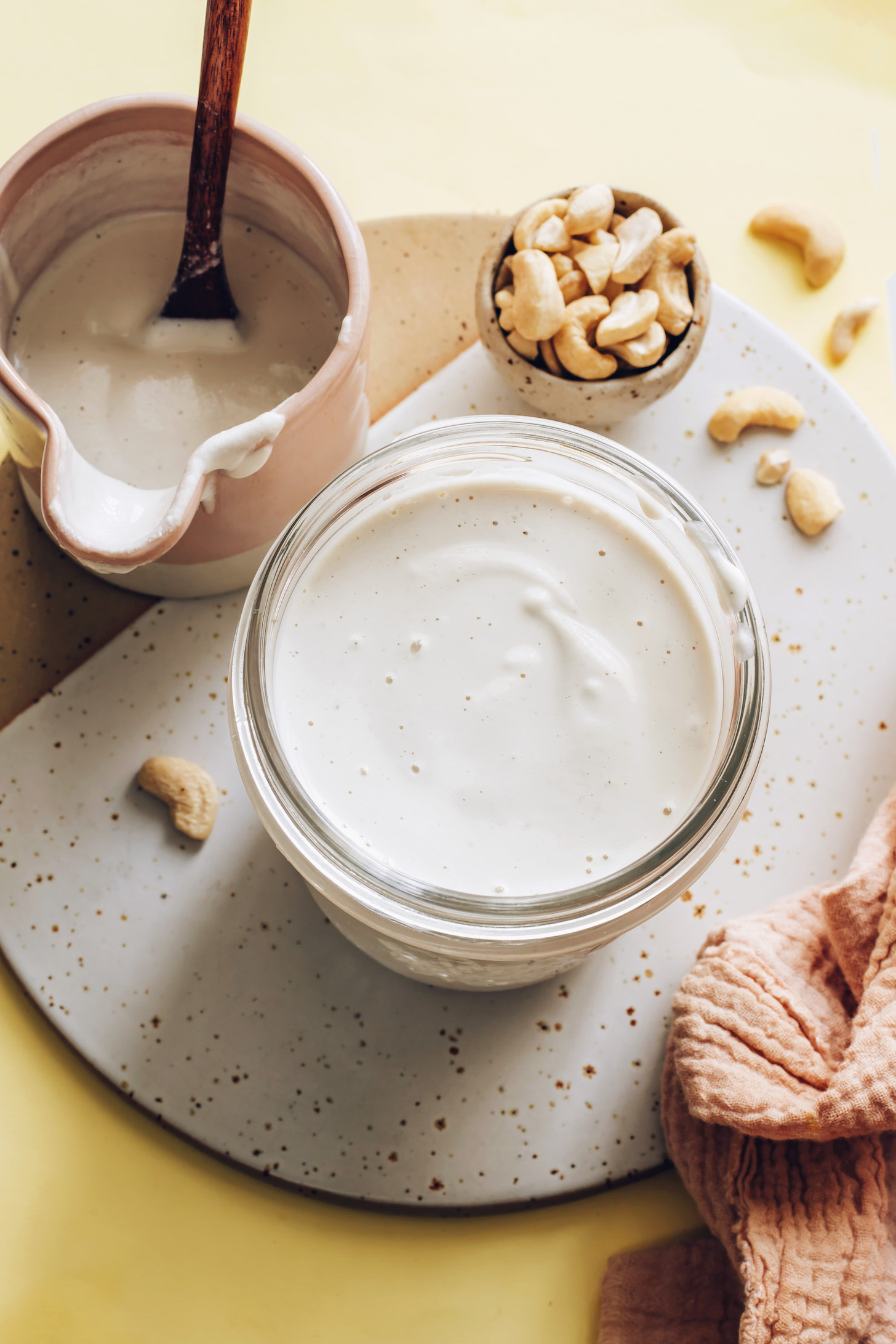 Jar and mini pitcher of cashew cream next to a bowl of raw cashews