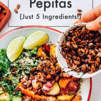 Hands sprinkling a bowl of chili lime roasted pepitas over a salad bowl