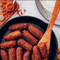 Cast iron skillet of vegan and gluten-free chorizo sausage links with a wooden spoon in it