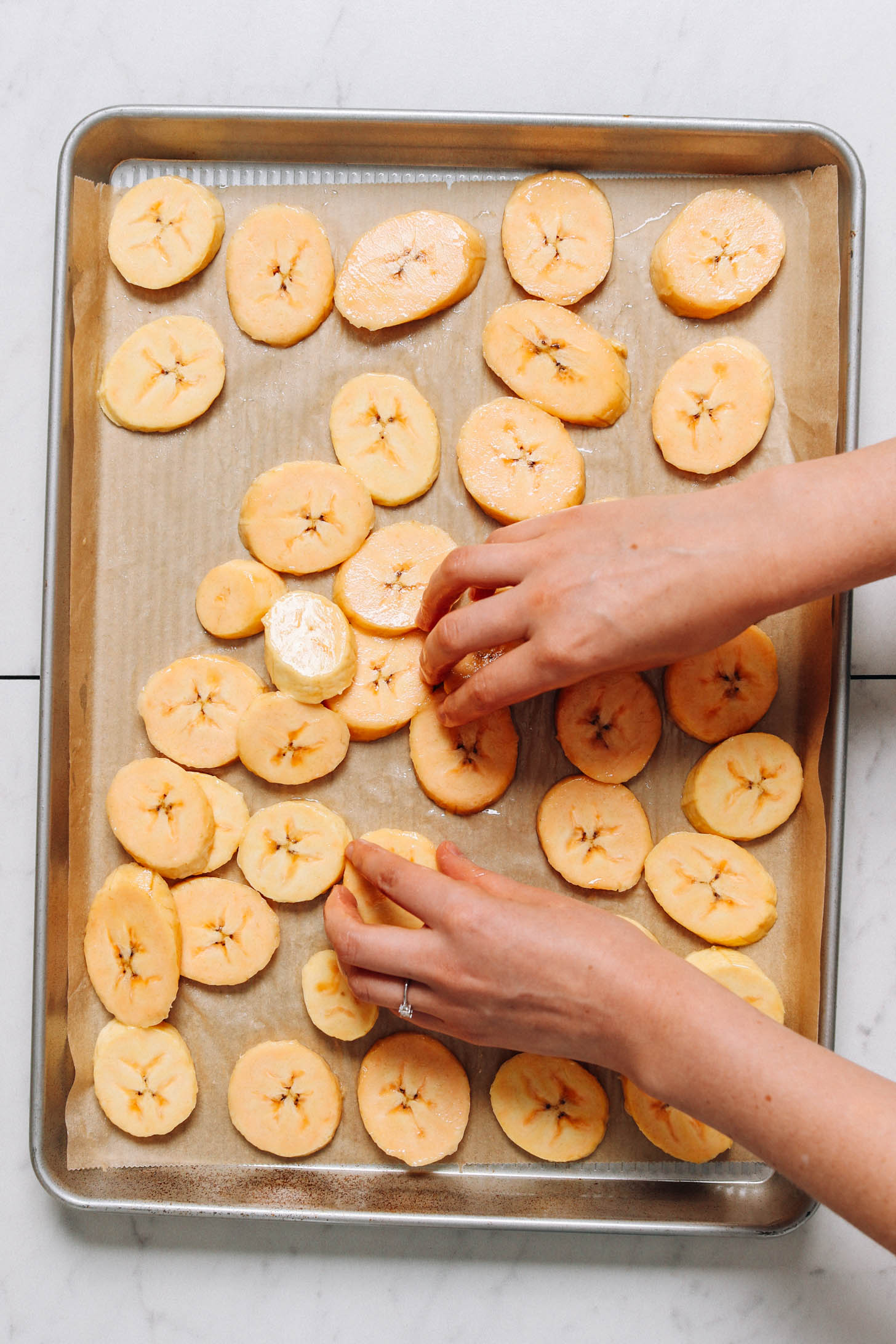 Arranging plantain slices on a parchment-lined baking sheet
