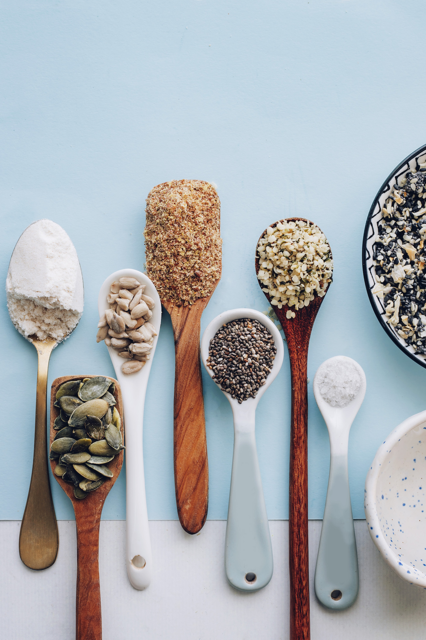 Spoonfuls of seeds and salt next to bowls of water and Everything Bagel Seasoning