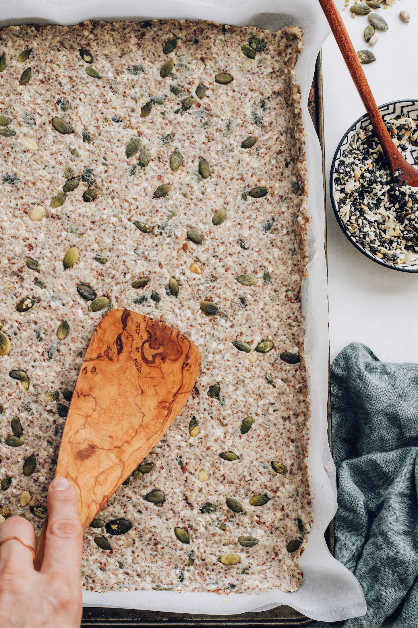 Spreading seed cracker dough into a parchment-lined baking sheet