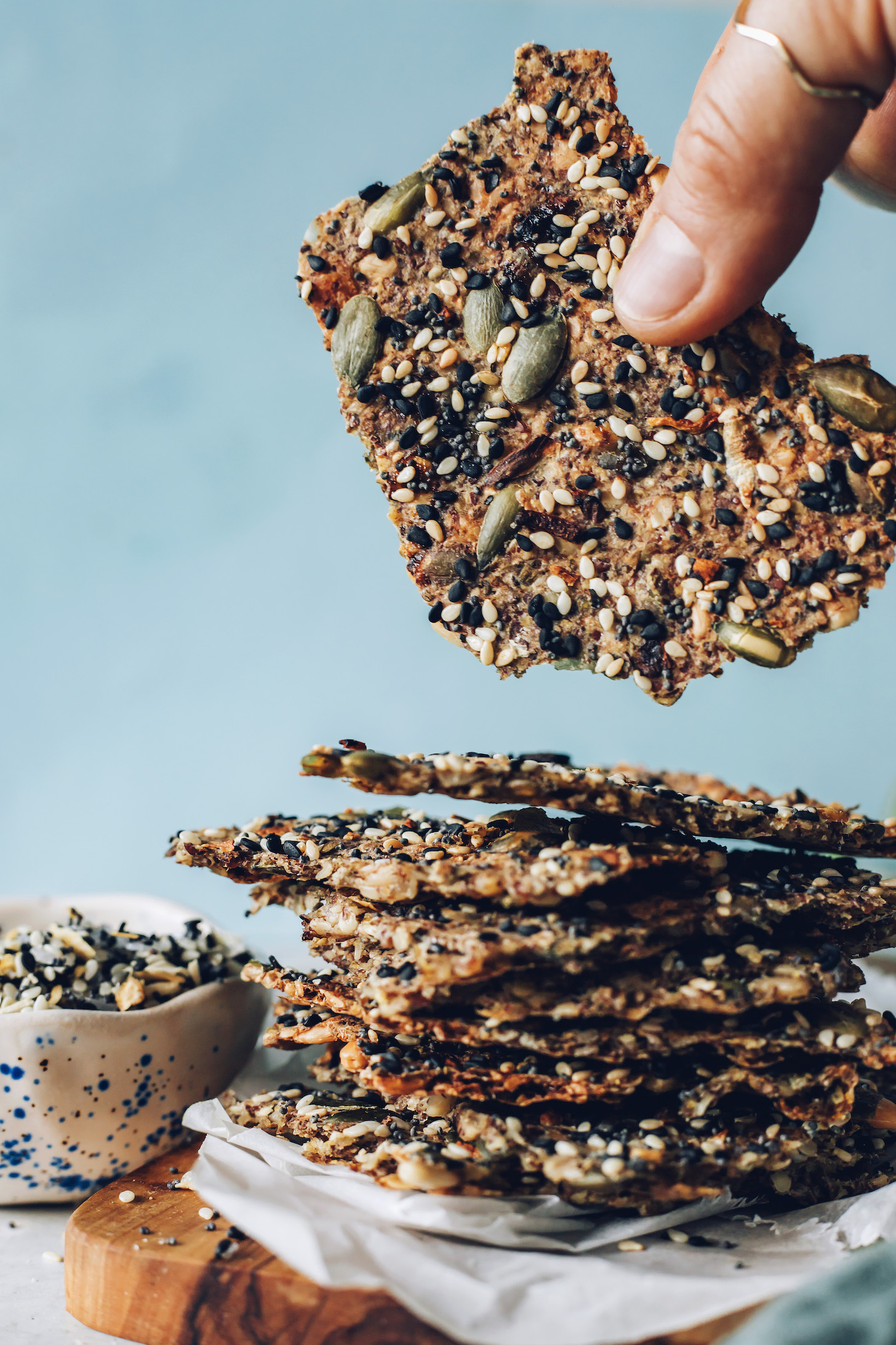 Holding up an everything bagel seedy cracker