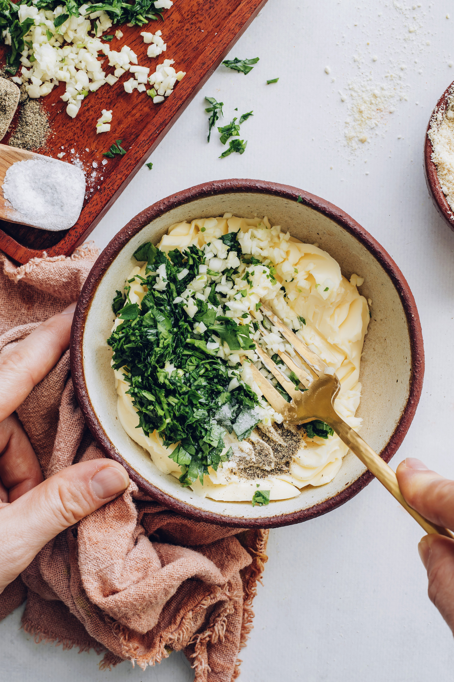 Using a fork to mix softened vegan butter, garlic, parsley, salt, and pepper in a bowl
