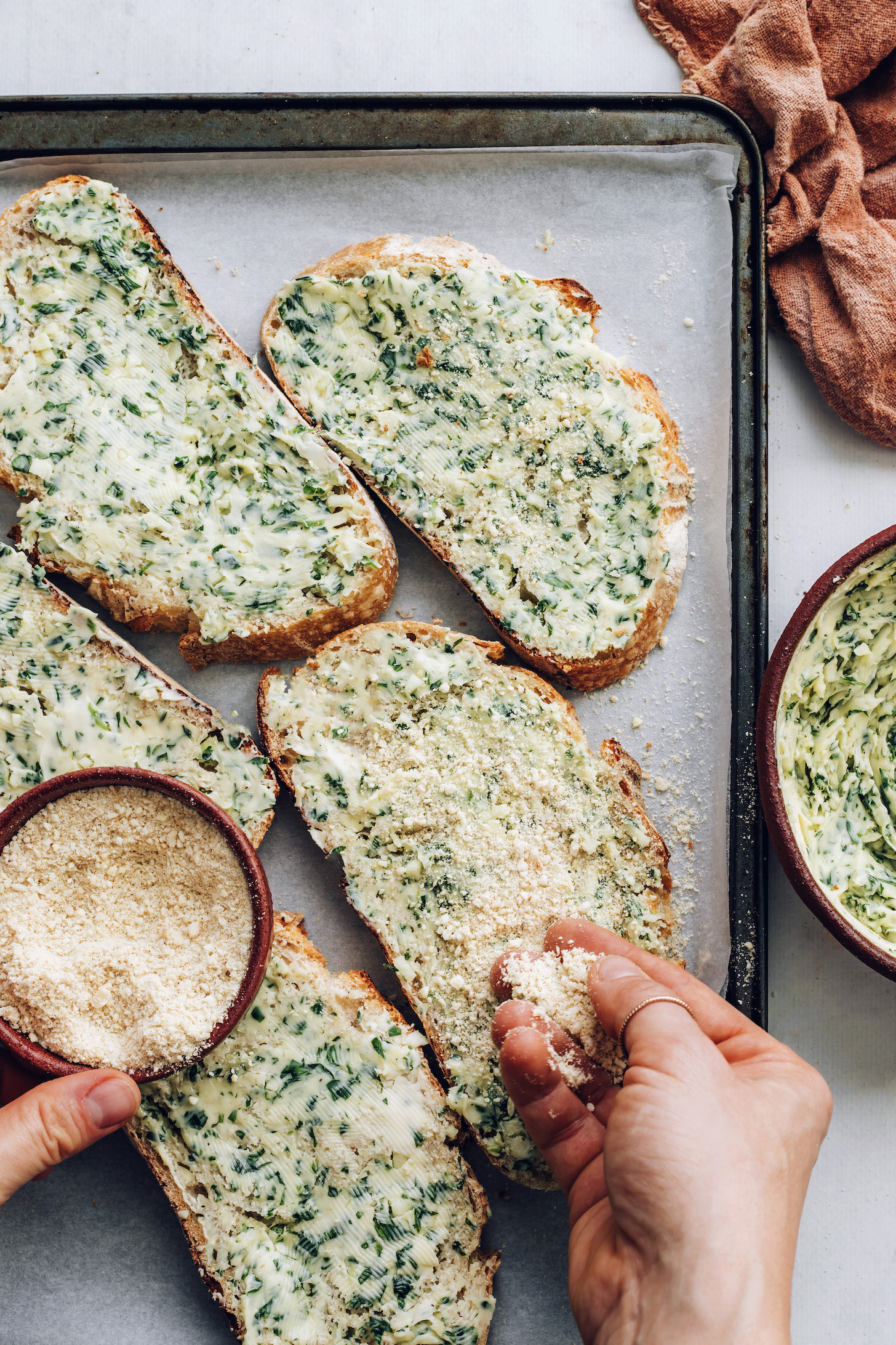 Sprinkling vegan parmesan cheese onto slices of garlic bread