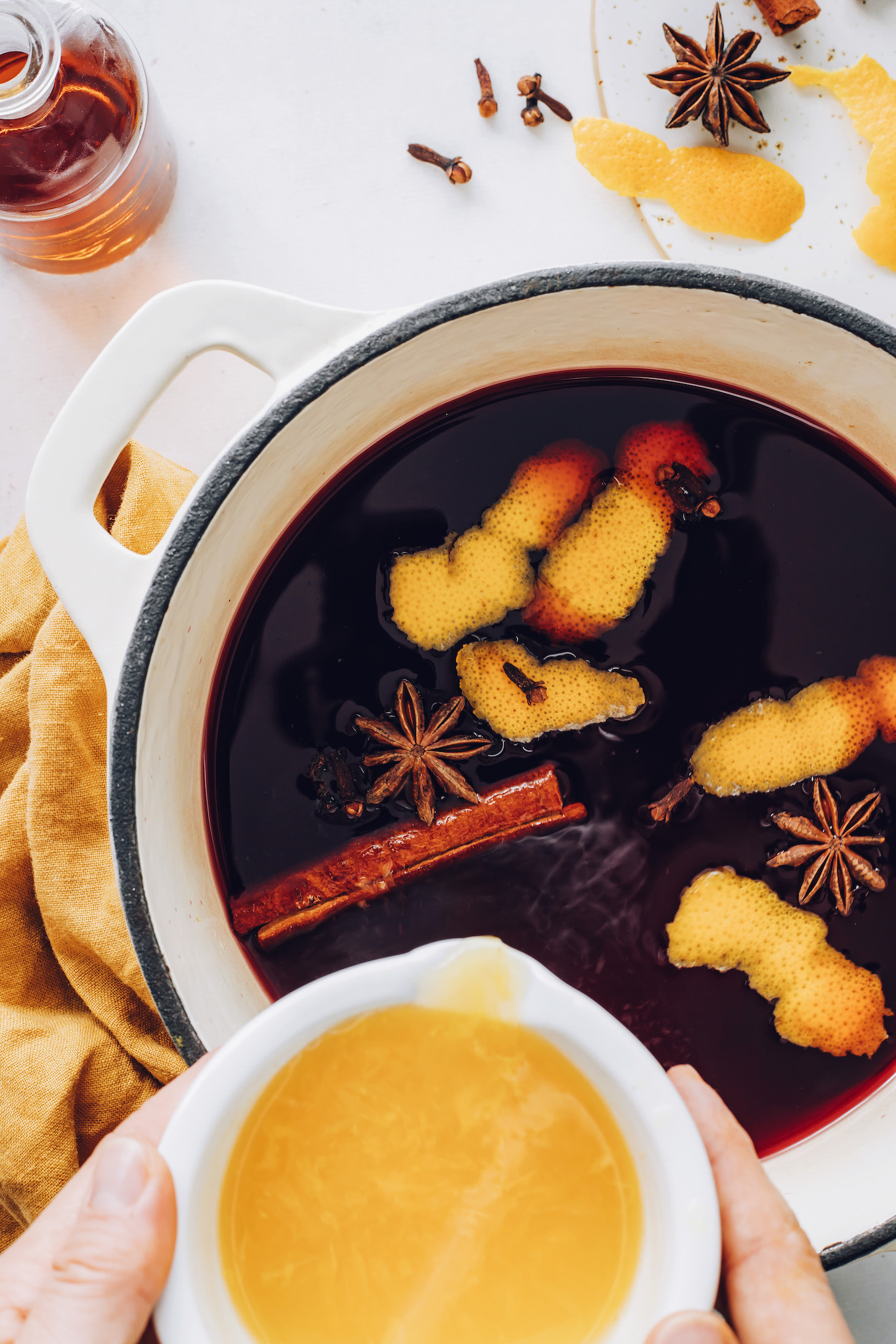 Pouring orange juice into a pot of tart cherry juice and spices