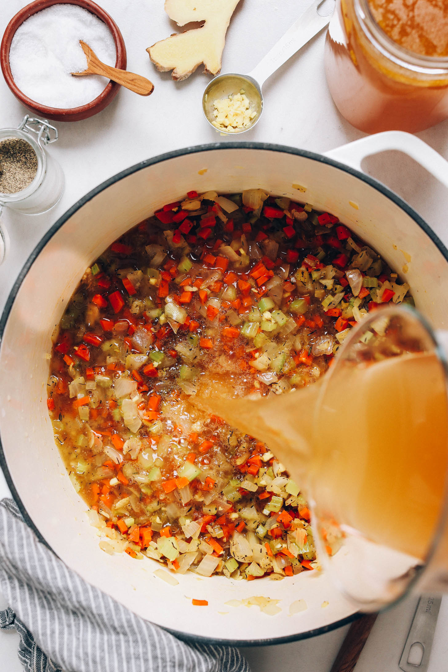 Pouring chicken stock over sautéed vegetables