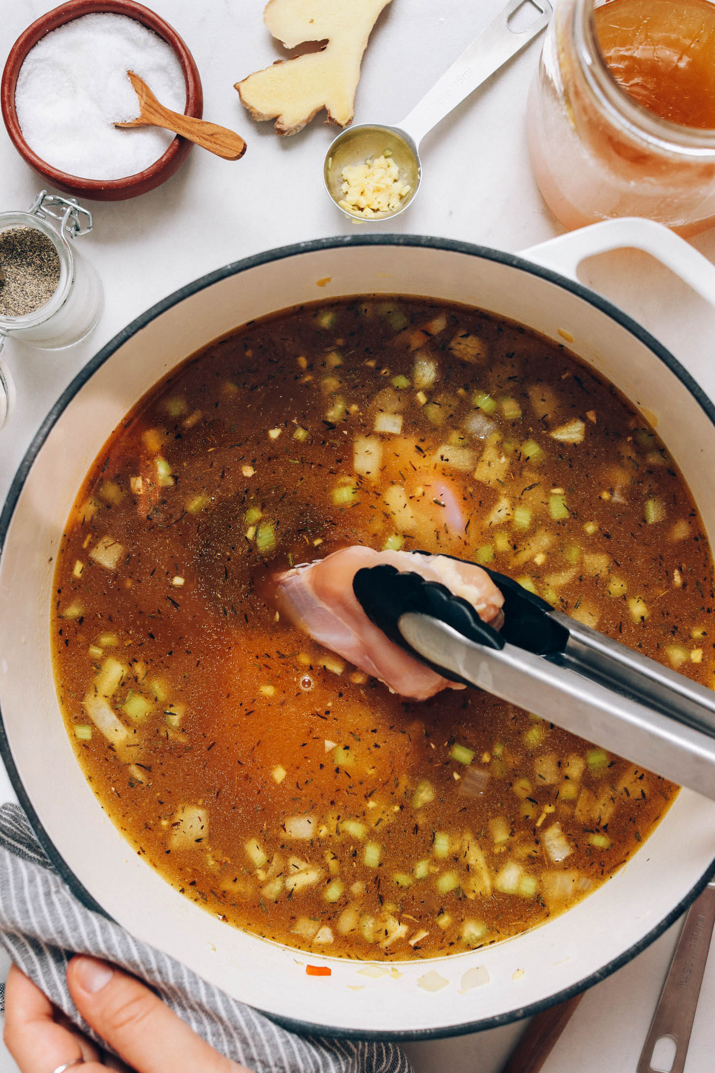 Using tongs to add boneless skinless chicken thighs to broth
