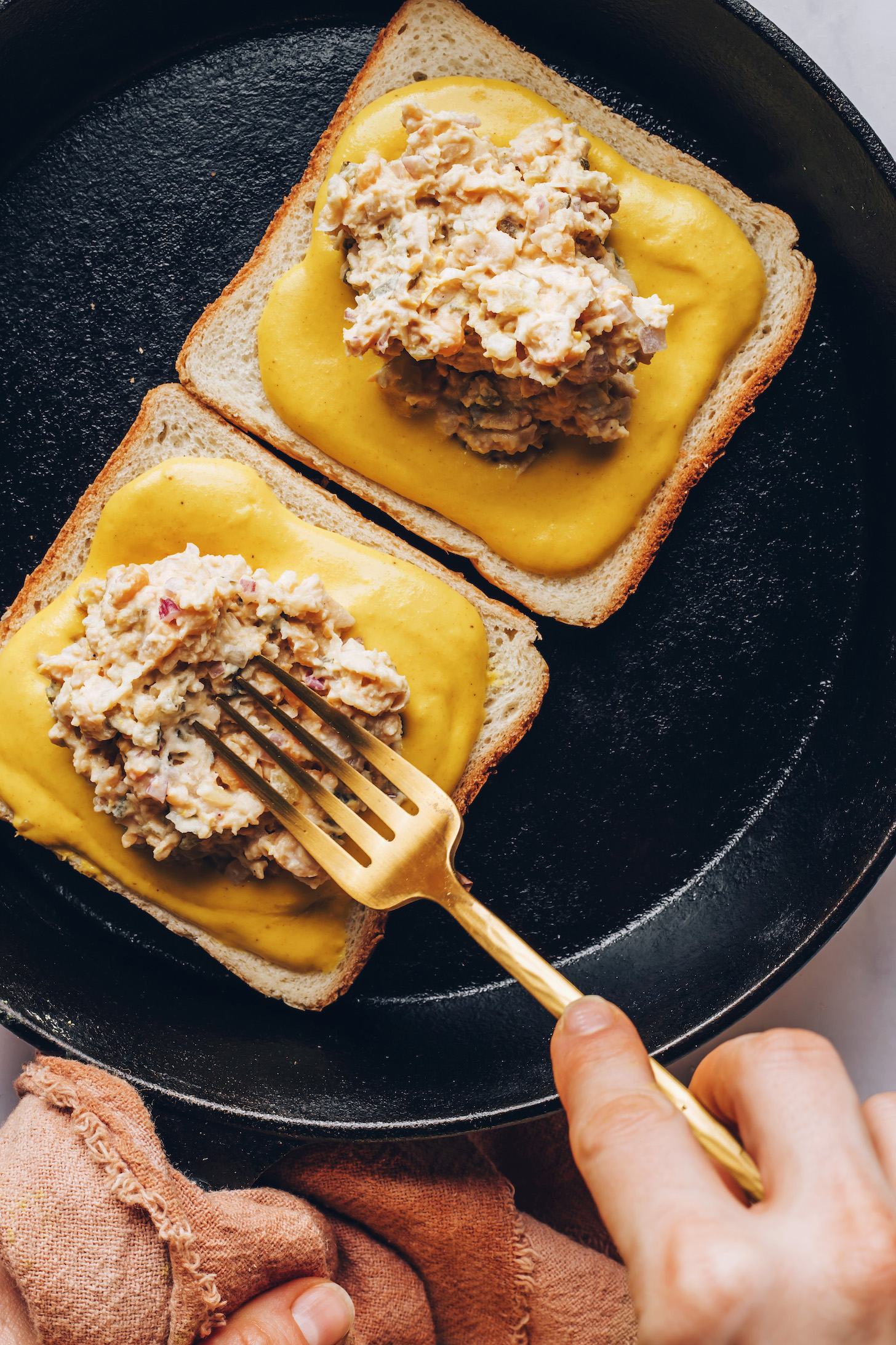 Skillet with slices of bread topping with vegan cheese and chickpea filling