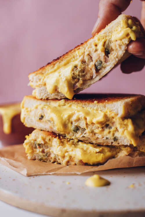 Picking up a vegan chickpea tuna melt from a stack of sandwiches