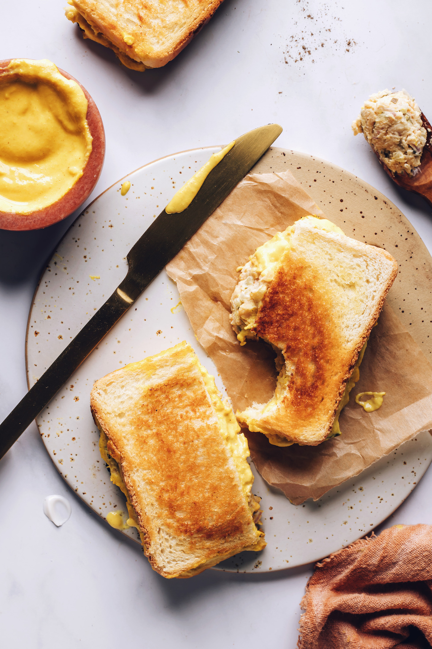 Bowl of homemade vegan cheddar cheese next to a vegan tuna melt