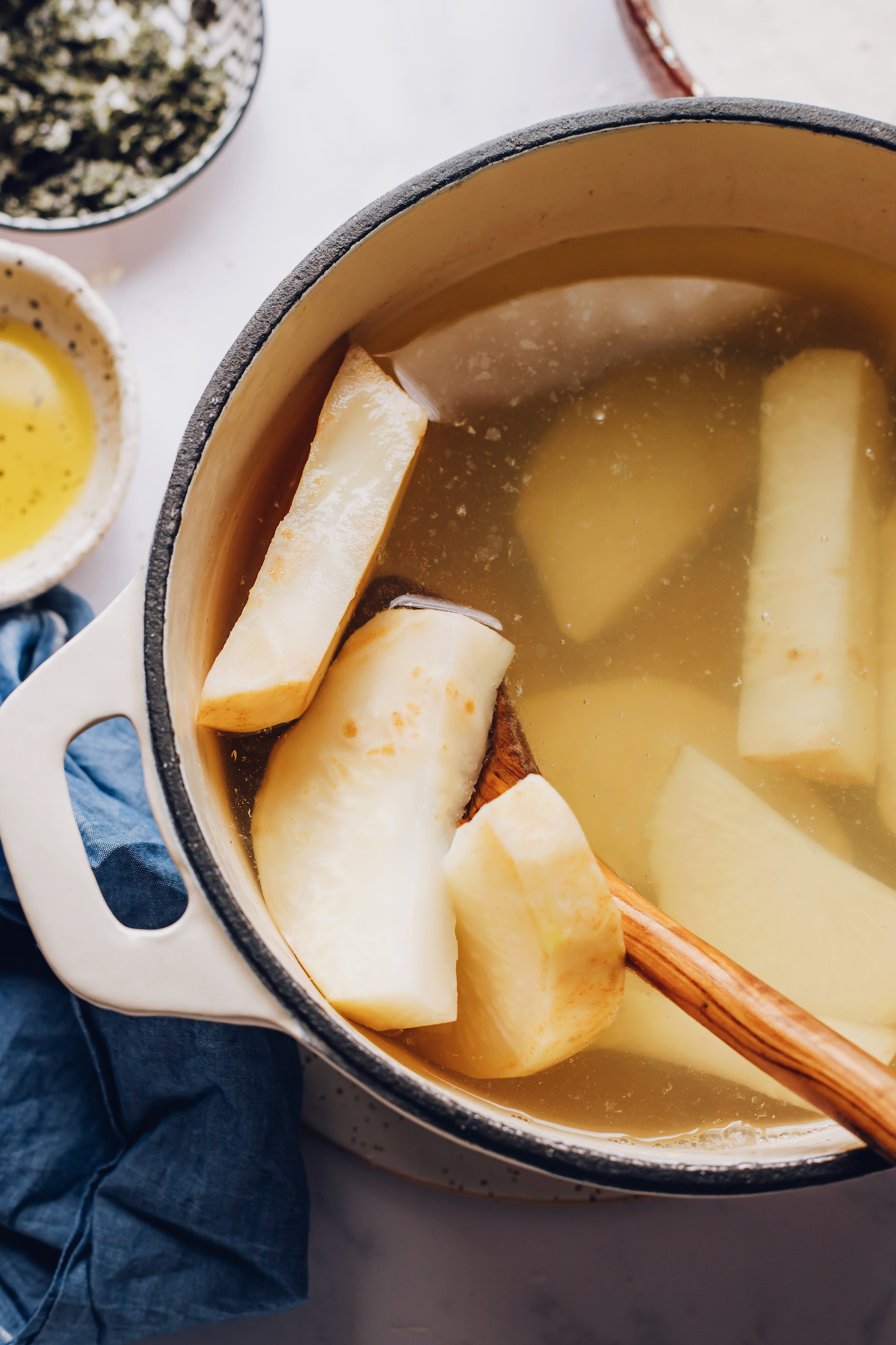 Using a wooden spoon to remove boiled celeriac wedges from a pot of water