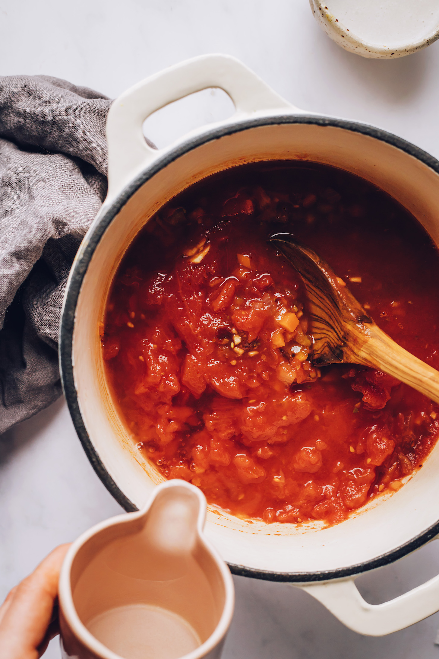 Adding water to a pot of sautéed veggies, tomatoes, and chipotle peppers