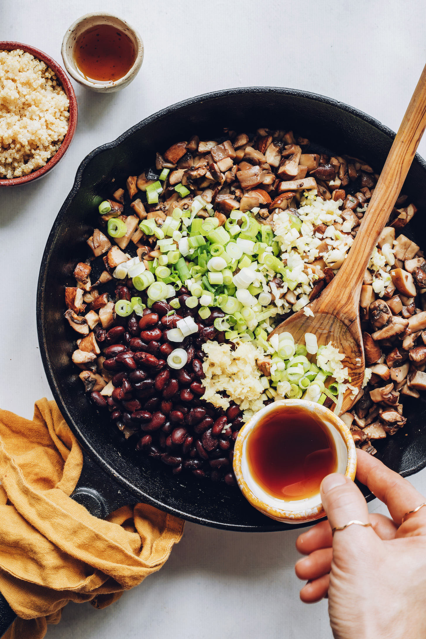 Pouring maple syrup over black beans, mushrooms, green onion, garlic, and ginger